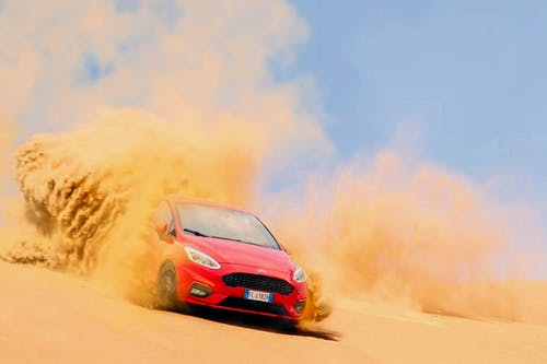 红色福特重点车辆在白天的蓝色天空下的沙子上驾驶 · 免费素材图片