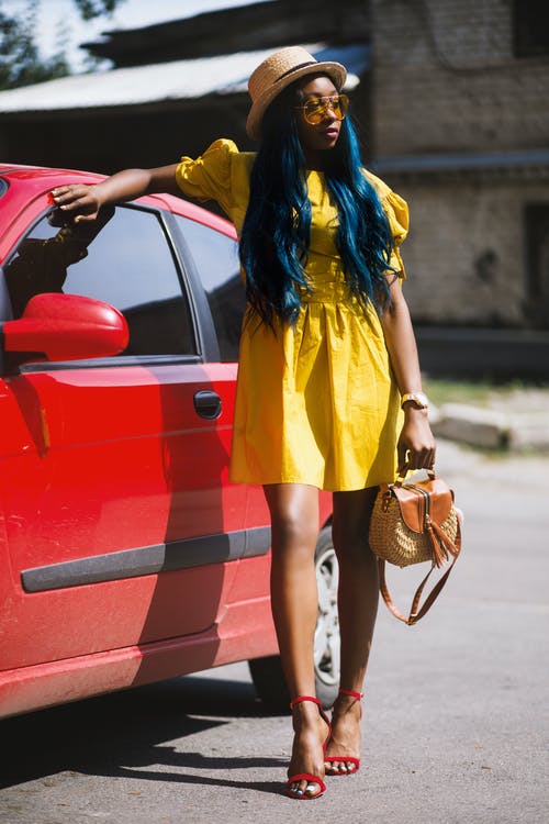 黄色的迷你连衣裙，拿着手提包在红色汽车旁边的女人 · 免费素材图片