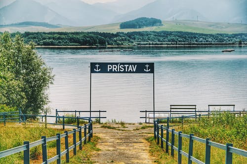 平静的水体旁的黑色金属标牌 · 免费素材图片