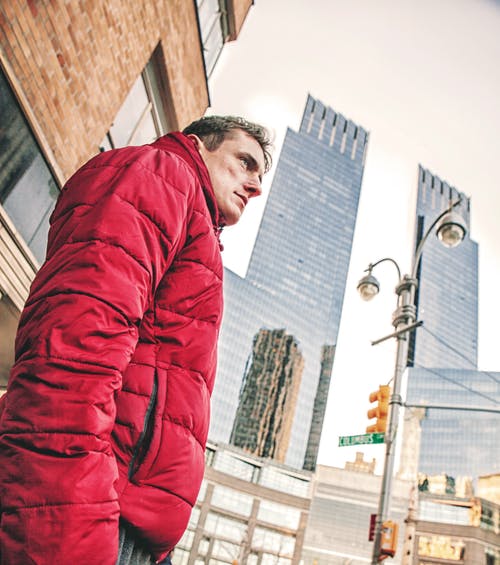 身穿红色泡泡大衣站在高层建筑下的男人 · 免费素材图片