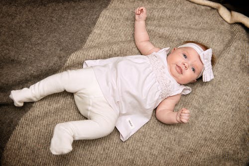 躺在灰色纺织品上的白色连衣裙的婴儿 · 免费素材图片