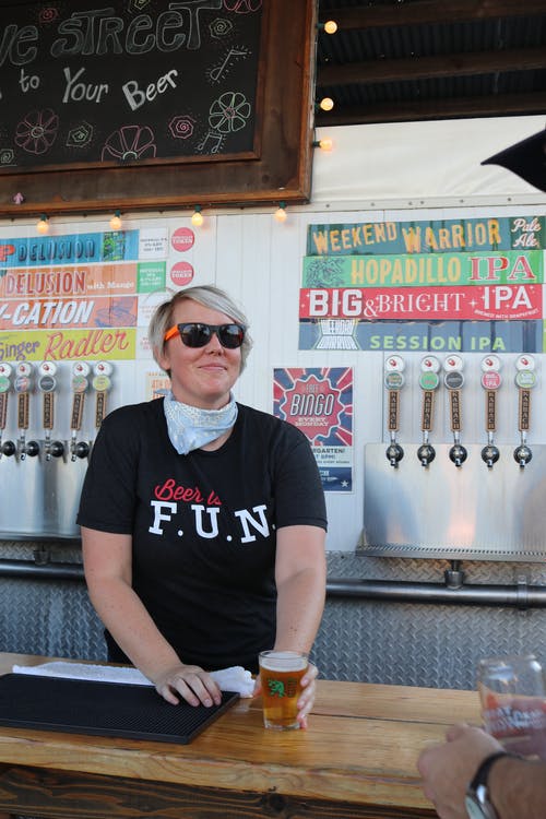 戴着黑色太阳镜的男子手持酒吧柜台内的透明啤酒杯 · 免费素材图片