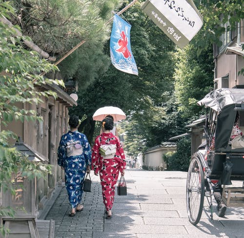 两个女人穿着和服走在人行道旁 · 免费素材图片