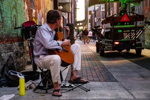 男人坐在灰色的路上弹古典吉他 · 免费素材图片