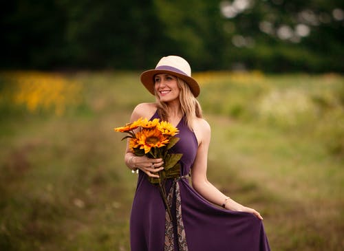 拿着向日葵花束的紫色礼服的微笑的妇女照片 · 免费素材图片