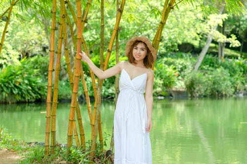 持有竹树在水体附近的白色意大利面条皮带礼服的女人 · 免费素材图片