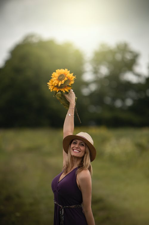举起向日葵花束的微笑女人的照片 · 免费素材图片