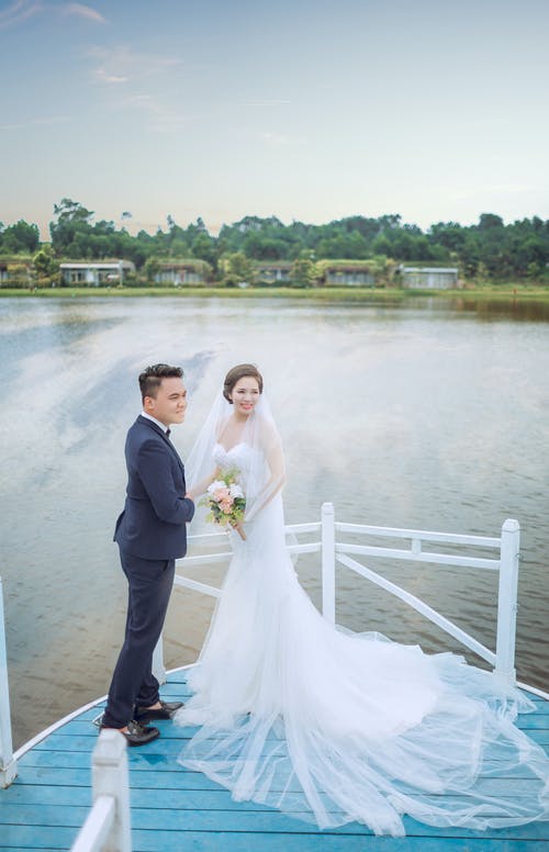 刚结婚的男人和女人在水体附近的蓝色平台上 · 免费素材图片