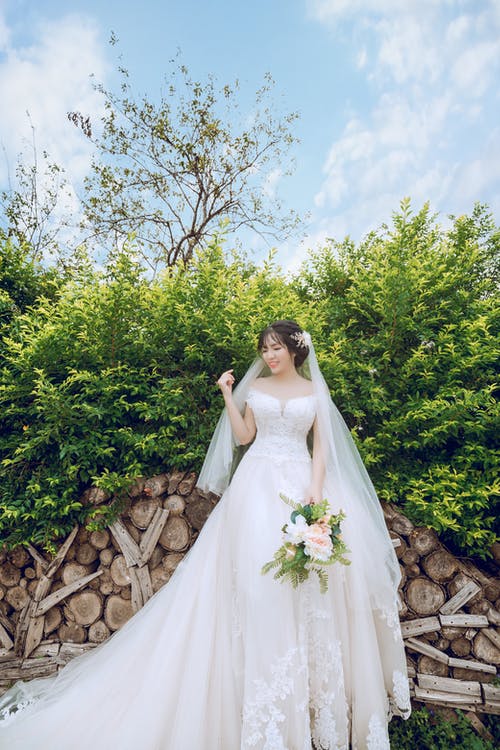 新娘捧着花束站在前绿叶植物 · 免费素材图片