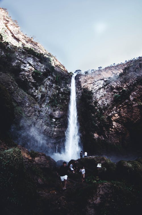 瀑布附近的棕色岩石上的人 · 免费素材图片
