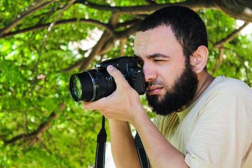 米色衬衫的男人在树旁边使用黑色的dslr相机拍照 · 免费素材图片
