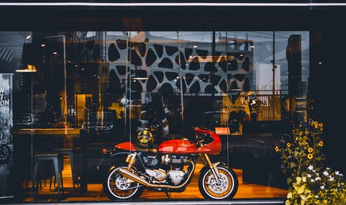 红色标准摩托车，玻璃墙附近有金头盔 · 免费素材图片