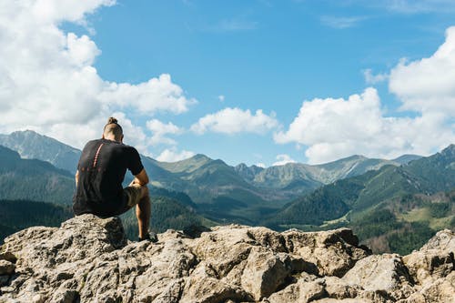 男子坐在山脉内的岩石上 · 免费素材图片