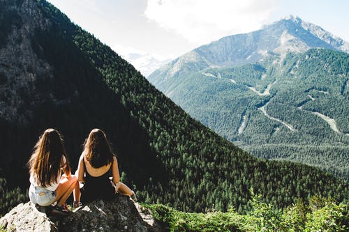 两个女人坐在面对岩石的山脉，在白多云的天空下 · 免费素材图片