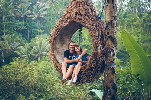 男人和女人坐在一棵树上的吊椅上 · 免费素材图片