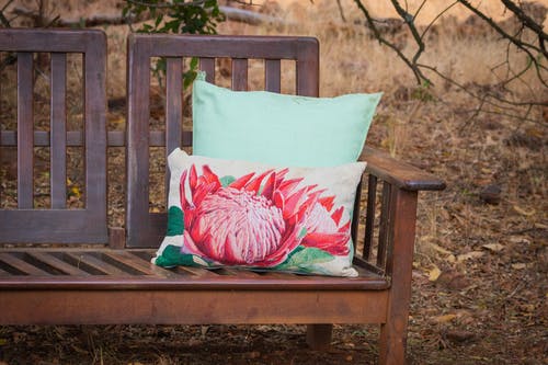 白色枕头与莲花印在公园的棕色木凳上 · 免费素材图片