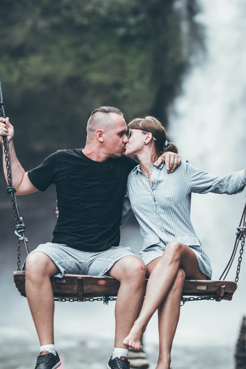 男人和女人在亲吻时坐在木秋千上 · 免费素材图片