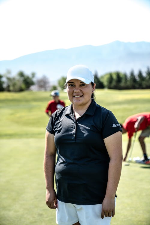 微笑着站在高尔夫球场上的女人 · 免费素材图片
