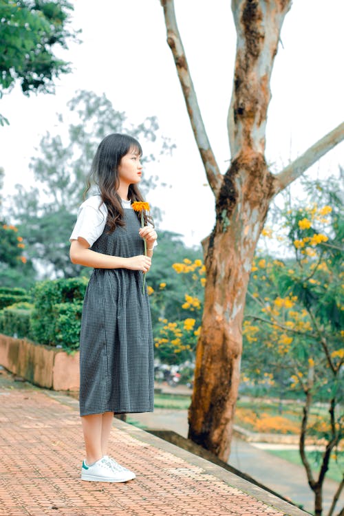女人拿着橙色的花瓣花的选择性焦点摄影 · 免费素材图片