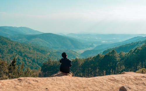 男子坐在悬崖上俯瞰山 · 免费素材图片