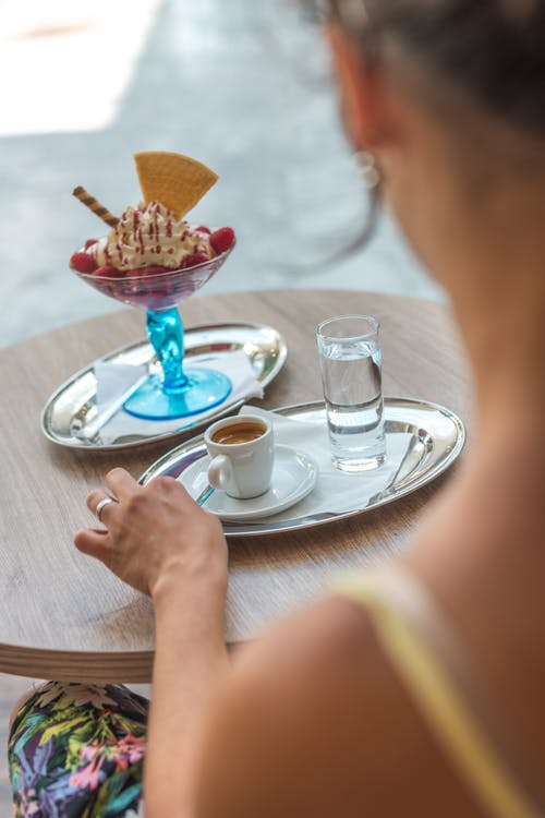 女人坐在椅子上，而她的左手在咖啡杯上灰色托盘旁边 · 免费素材图片