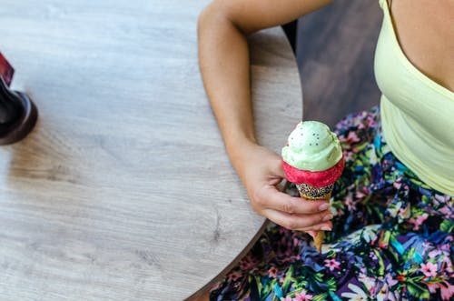 女人坐在桌子旁拿着冰淇淋的同时坐 · 免费素材图片