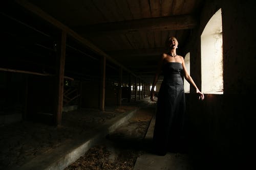 女人穿着黑色露肩礼服站在窗户附近 · 免费素材图片