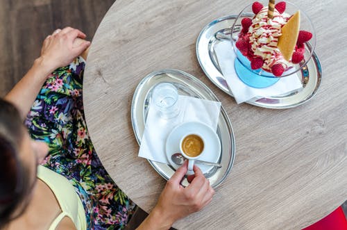 拿着茶杯在盘子上时坐在木桌前的人 · 免费素材图片