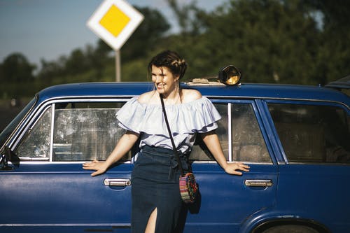 女人触摸蓝色车时穿白色的露肩上衣 · 免费素材图片
