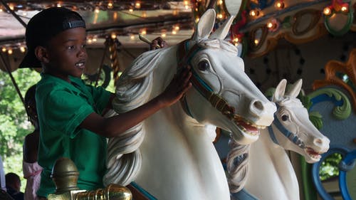 男孩穿着绿色polo衫骑旋转木马 · 免费素材图片