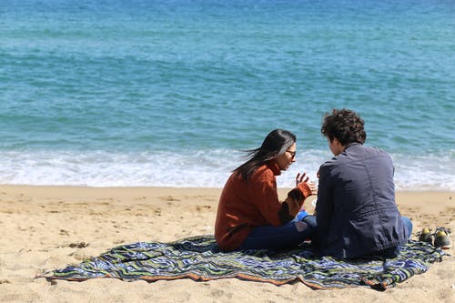 男人和女人坐在海滩附近 · 免费素材图片