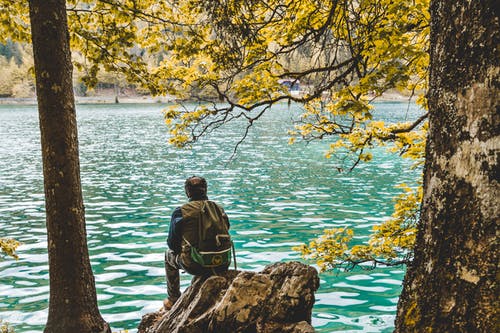 男子坐在湖边的岩石上的照片 · 免费素材图片