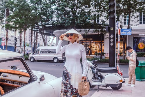 女人穿着白色的衣服，站在一辆车停在路边 · 免费素材图片