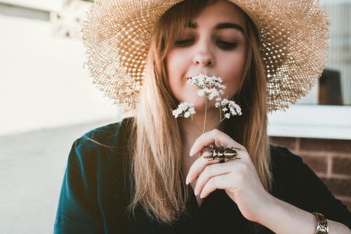 女人戴着棕色的太阳帽闻到白花 · 免费素材图片