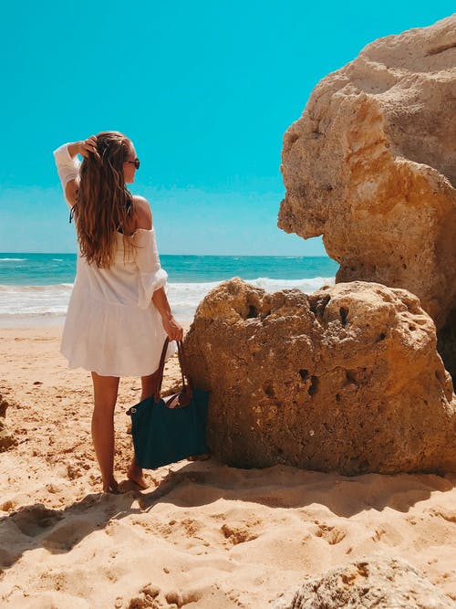 女人站在海滩附近的岩石旁边 · 免费素材图片