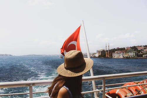土耳其国旗和水体附近戴棕色太阳帽的女人 · 免费素材图片