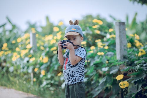 拿着照相机在黄色花前面的男孩 · 免费素材图片