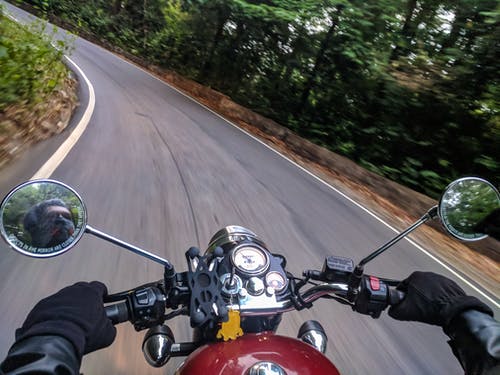 在树木附近的弯曲混凝土道路上驾驶摩托车的人 · 免费素材图片