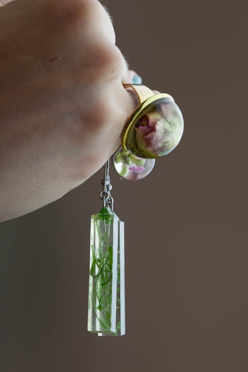 拿着矩形绿叶镇纸吊坠时戴金色花泡泡戒指的人 · 免费素材图片