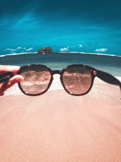 拿着太阳镜在海滩前的人 · 免费素材图片