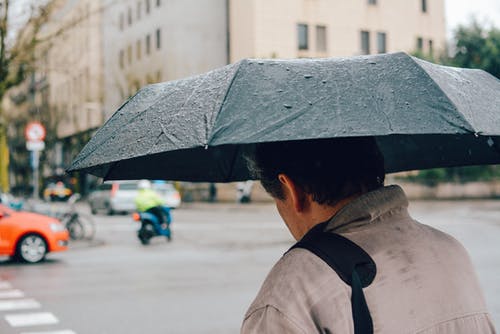 男子手持黑色折叠伞走在街上 · 免费素材图片