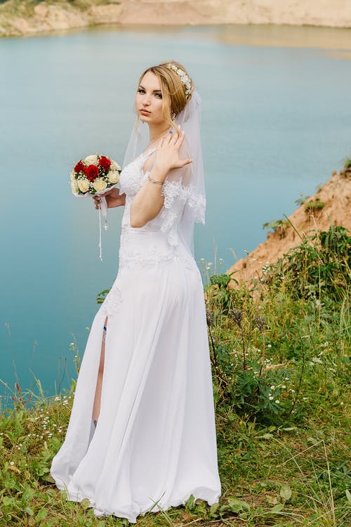 女人站在河边的悬崖上穿着白色的婚纱 · 免费素材图片
