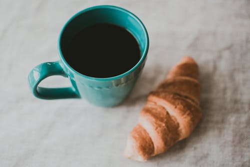 蓝绿色陶瓷杯装满咖啡，烤面包附近 · 免费素材图片