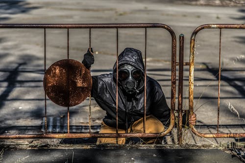 戴着防毒面具的人坐在金属栅栏后面 · 免费素材图片