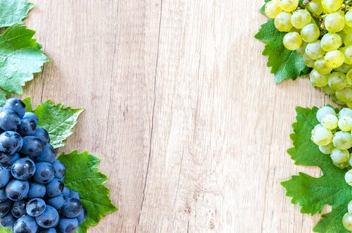 米色木质表面上的蓝色浆果和绿色葡萄 · 免费素材图片