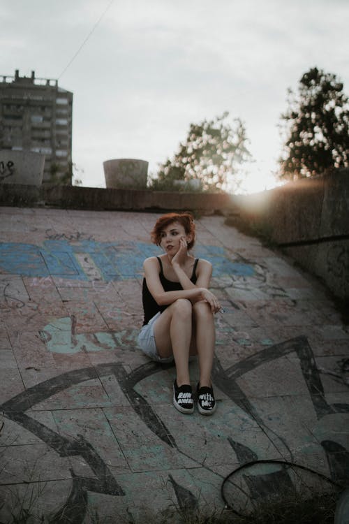 女人穿着黑色背心坐在混凝土表面 · 免费素材图片