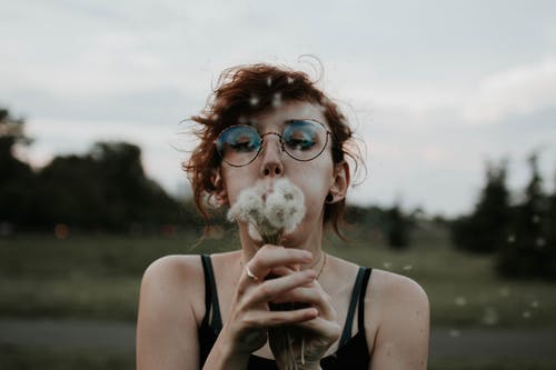 女人吹蒲公英花的选择性聚焦摄影 · 免费素材图片