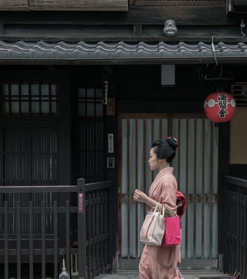 女人穿着粉红色的和服走在房子附近 · 免费素材图片