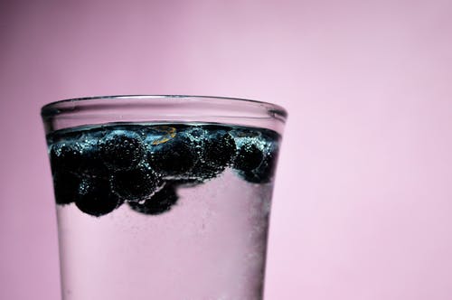 清晰的水杯与浮动蓝莓的特写摄影 · 免费素材图片