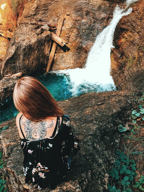 女人坐在瀑布上的岩石 · 免费素材图片